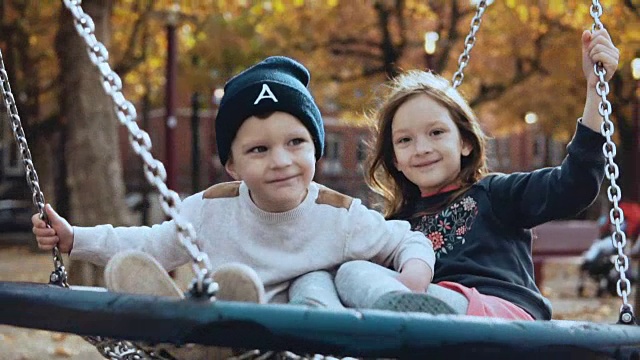 两个小孩在公园里的秋千上荡秋千。欧洲的孩子们看着镜头笑得很开心视频素材
