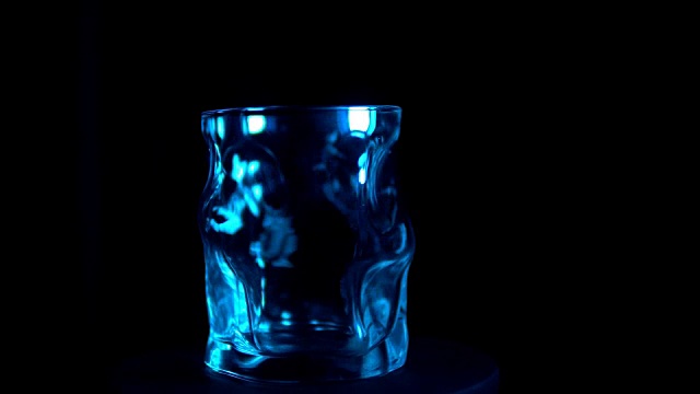 玻璃酒杯在黑色背景的蓝色背光下转动视频下载