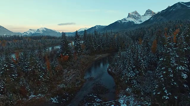空中(无人机)的景象，覆盖着积雪的常绿植物，河流，和山在日落视频素材