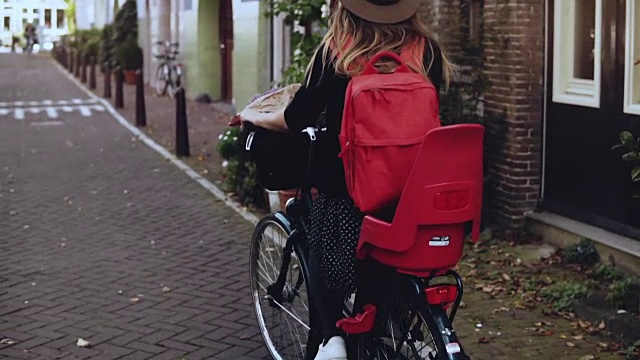 后视图。自行车上背着红色背包的女性。缓慢的运动。兴奋的白人女游客。生活美容博客视频素材