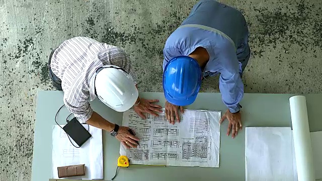 俯视图的工程团队的现场经理和现场工程师在施工现场看已构建的图纸计划。为重工业团队合作的经营理念。视频素材