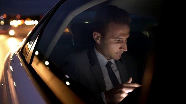 微软商人在一辆豪华轿车里使用平板电脑在夜晚的城市里视频素材