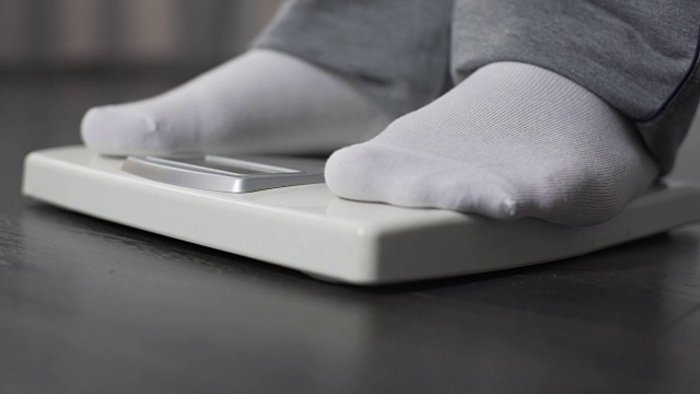 肥胖男子在健康秤上测量自己的体重，节食和减肥，特写视频下载