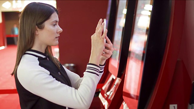 青少年在电影院的自动贩卖机购买电影票。女人用手机拍照视频素材