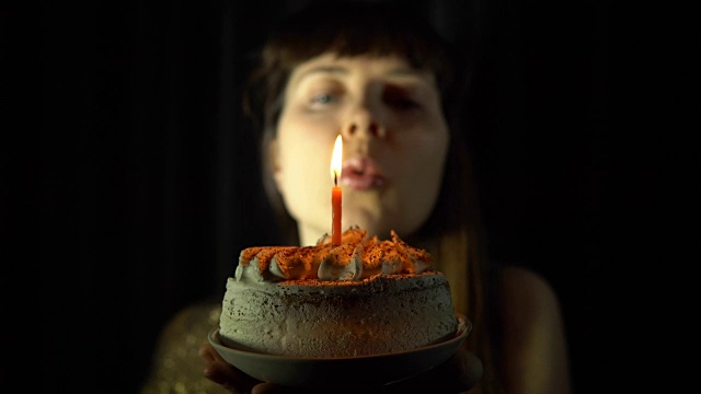 一个女人吹灭一个黑色背景上的蛋糕上的蜡烛的特写。视频素材