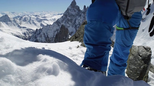 在阳光明媚的日子里，登山者在多雪的山顶附近使用冰斧。登山滑雪活动。滑雪者冬季在高山户外进行滑雪运动。后视图。慢动作60p 4k视频视频素材