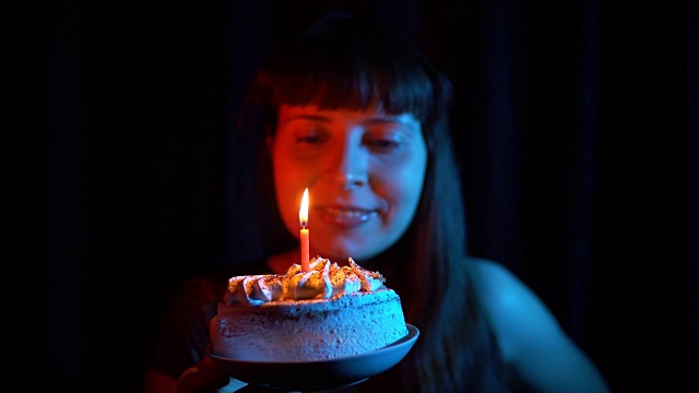 一个女人吹灭一个黑色背景上的蛋糕上的蜡烛的特写。视频素材