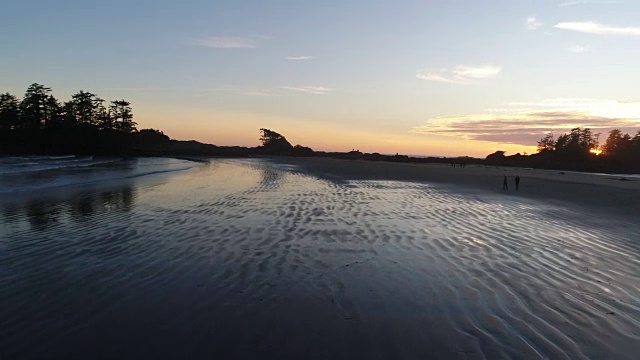 一名女子在日落时分在太平洋附近的海滩上散步的航拍镜头视频下载