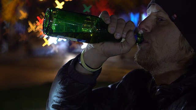 年轻人坐的特写，看着夜晚的街道和喝啤酒的瓶子视频下载