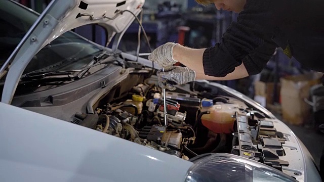 一个年轻人正在旋转的工具的帮助下，发动机从一个汽车技工正在修理汽车，以使它顺利进行视频素材