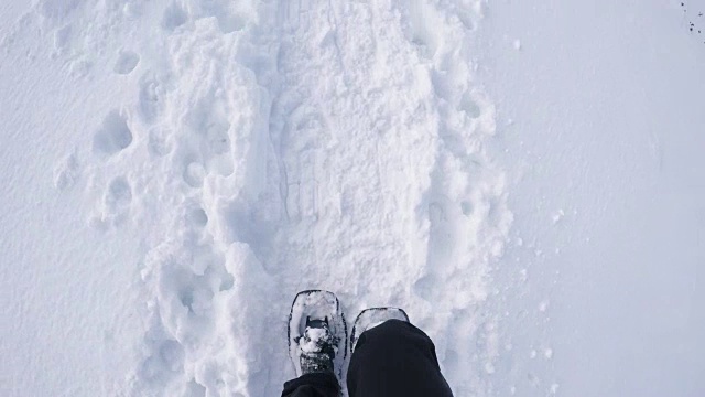 头顶上的POV人徒步行走，穿着雪鞋，在冬天的野外白雪皑皑的小路上。腿和鞋在雪地上踏的细节。视点4k视频视频素材