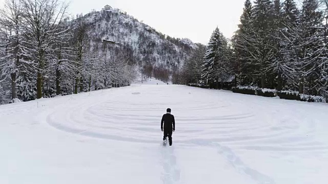 在多云的冬天，人们穿着雪鞋在松树林附近的白雪覆盖的山上行走。欧洲阿尔卑斯山户外自然景观雪山。回来后。4 k无人机飞行视频素材