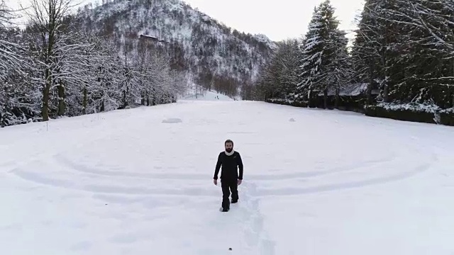 在冬季，在松林附近的雪地上，人们穿着雪鞋向后空中行走。欧洲阿尔卑斯山户外自然景观雪山。前面跟着徒步的人们。4 k无人机飞行视频素材