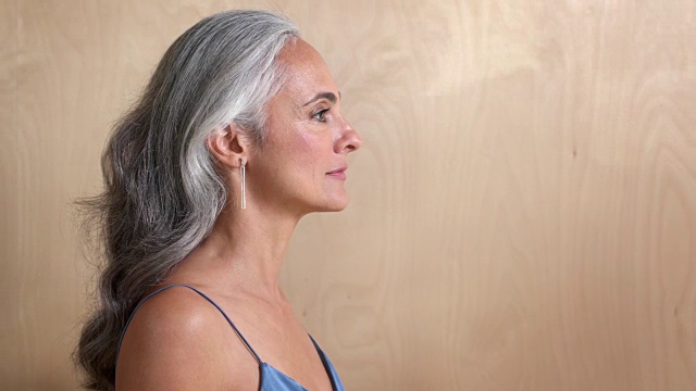 一名灰白头发的中年妇女对着镜头微笑，背景是一堵木墙。视频素材
