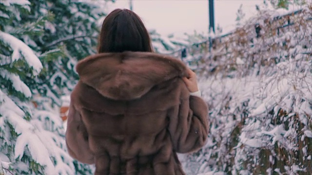 深褐色的女孩穿着棕色的毛皮大衣在冬天慢动作的走着视频下载