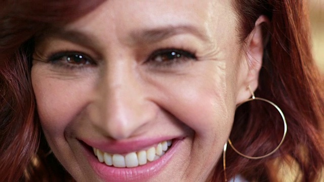 一个红色头发的中年妇女在镜头前微笑的极端特写，在一个模糊的背景。视频下载