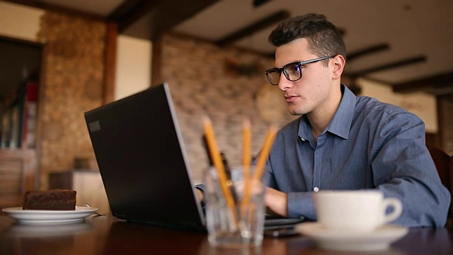英俊的自由职业者，戴着眼镜，在咖啡馆用笔记本电脑努力工作。一个人在键盘上打字，在网吧上网找新工作。经营理念视频素材