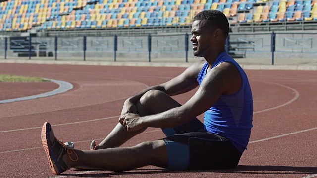 穿着运动服的男子坐在跑道上，在锻炼后恢复体力视频下载