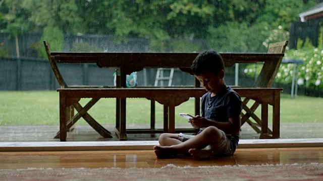 下雨的时候，男孩在玩手机视频素材