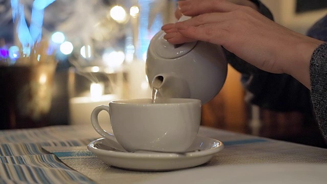 近女用手将热茶从茶壶里倒进白色的茶杯里。视频下载