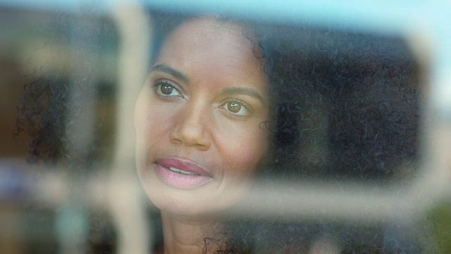 一个混血的中年妇女的肖像，自然的头发，微笑着看着窗外。视频下载