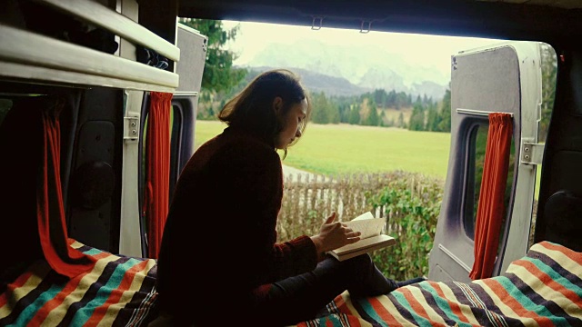 一个女人在露营车里看书，可以看到阿尔卑斯山视频素材