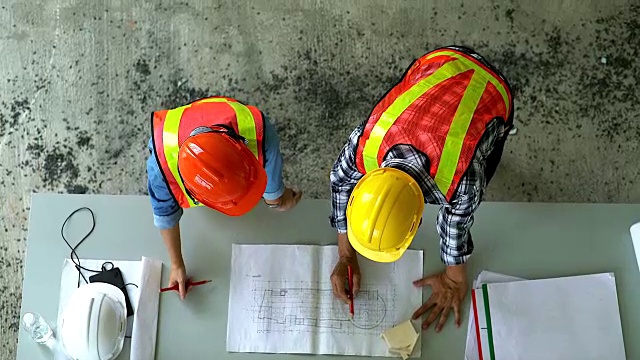 工程师和工地经理在施工现场看图纸的俯视图。为重工业团队合作的经营理念。视频素材