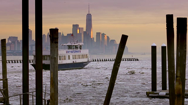 夕阳映照下曼哈顿下城的天际线，一艘纽约水路渡轮正驶过结冰的哈德逊河。视频素材