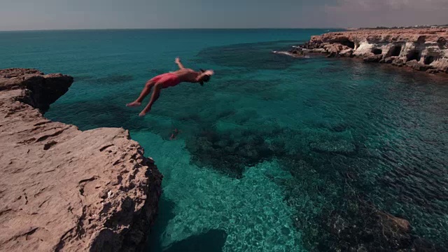 年轻的悬崖跳水者翻着筋斗从岩石上跳到海里视频素材