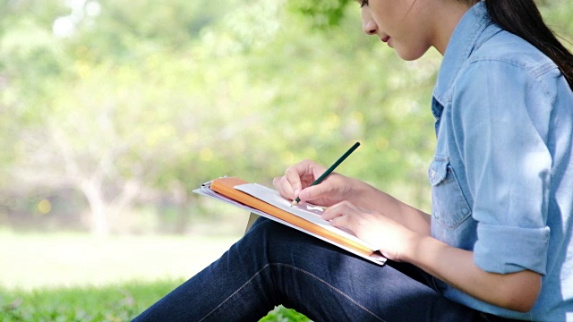 在绿春公园的户外散步中寻找灵感。特写的年轻女子的手写下她的希望和未来的梦想到她的日记，制定计划。计划去做视频素材