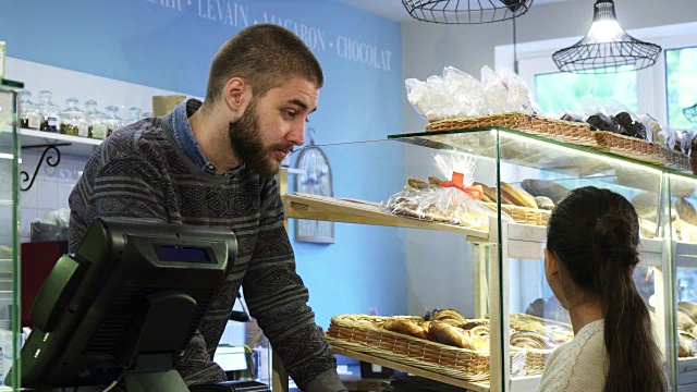 年轻的男面包师在他的店里帮一个小女孩选甜点视频素材