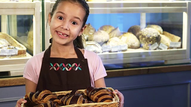 可爱的小女孩穿着围裙在面包店工作，对着镜头微笑视频素材