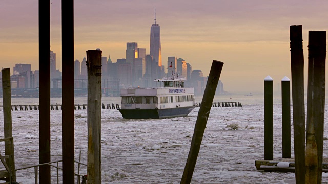 夕阳映照下曼哈顿下城的天际线，一艘纽约水路渡轮正驶过结冰的哈德逊河。视频素材