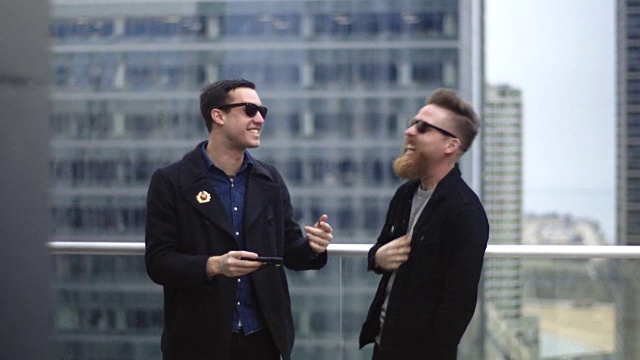 芝加哥高楼的阳台上，两个朋友一边看手机一边笑。视频下载