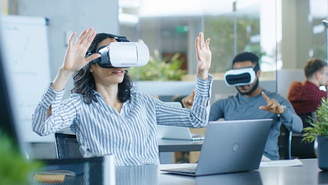 佩戴虚拟现实头盔的女性虚拟现实工程师/开发人员与同事一起创建内容。聪明的年轻人致力于增强和混合现实项目。视频素材