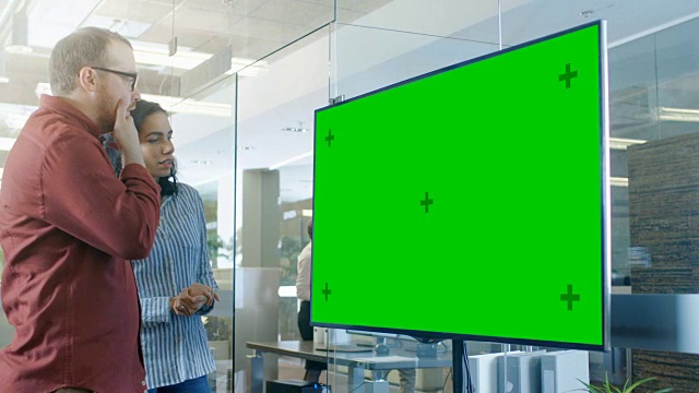 男、女在会议室讨论彩色键绿屏电视样机。视频素材