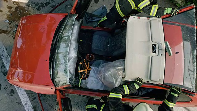 两名消防队员从一辆被撞坏的汽车的车顶上走下来，他们用液压切割器切割汽车视频素材