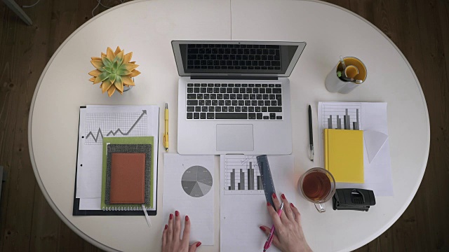 一位女士正在处理商业图表和一台放在白色桌子上的笔记本电脑，上面放着几杯茶。前视图。手关闭视频下载