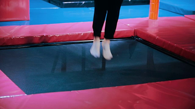 年轻的女杂技演员表演杂技戏法-在蹦床大厅，慢动作跳跃视频下载