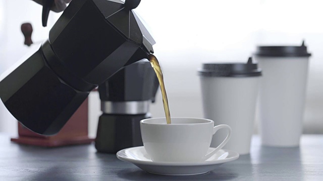 咖啡倒在一个杯子在一个蓝色的木制桌子背景与白色的咖啡杯，咖啡豆研磨机，间歇泉视频下载