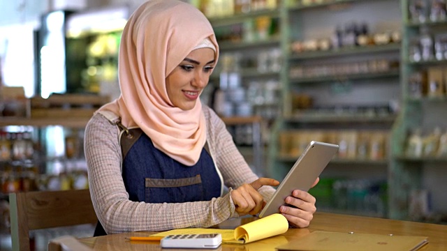 快乐的穆斯林企业主使用平板电脑和记事本，看起来非常满意和微笑视频下载