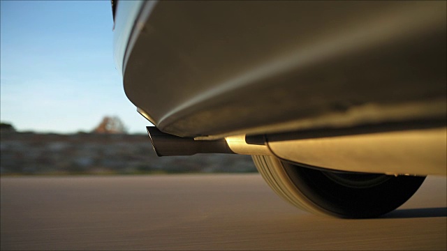 一辆德国车在日落时拍摄的视频，摄像头安装在后保险杠下方，排气管和左后轮轮胎突出在画面中，背景是运动模糊的视频素材