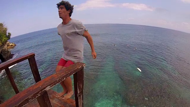 一个男人做了一个后空翻和悬崖跳进绿色的大海去冲浪。视频下载