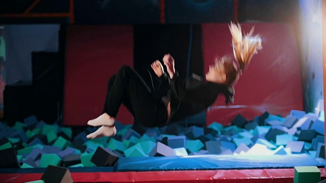 年轻的女杂技演员表演杂技戏法-在蹦床大厅，慢动作跳跃视频下载