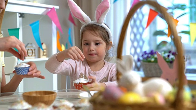 年轻的母亲和她的小女儿戴着滑稽的兔子耳朵做复活节纸杯蛋糕视频素材