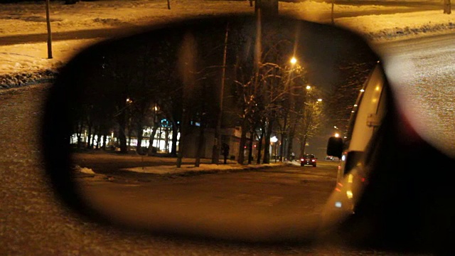 汽车和行人都反射在汽车的侧视镜上，在晚上的城市街道上。视频下载