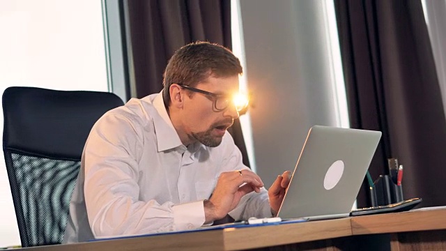 一个商人一边在笔记本电脑上打字，一边开心地微笑着。视频素材