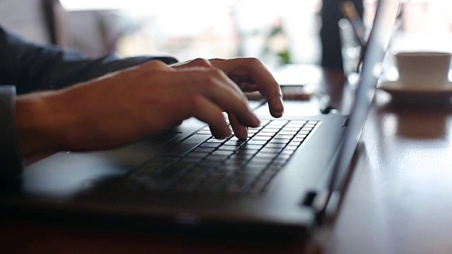 镜头在自由职业者在笔记本电脑键盘上打字的手周围以慢镜头移动。利用互联网在办公室工作的商人。背景是一杯咖啡。经营理念视频素材