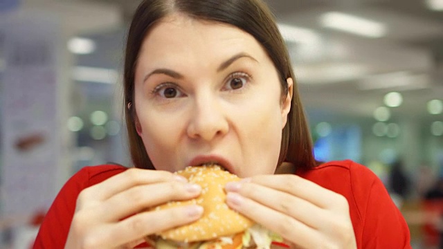 很饿的女孩在美食广场吃汉堡。在快餐店里咬着芝士汉堡的女人视频素材
