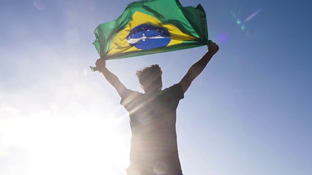 日落时分，在巴西的海滩上，一个年轻人双手举着巴西国旗升天视频素材